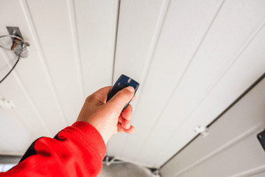 Hand holding a garage door remote up to the motor unit on the ceiling track